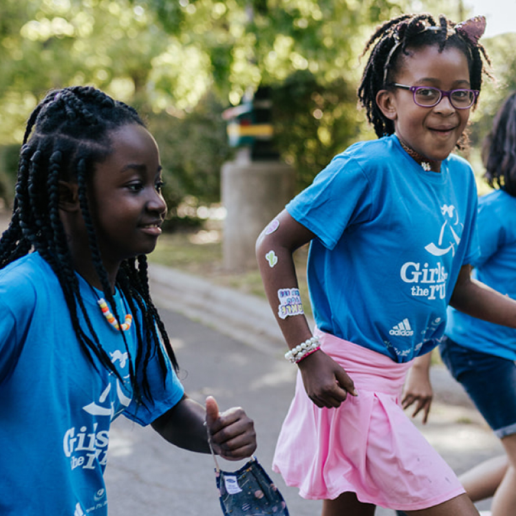 Two Girls on the Run participants in blue shirts smile while running at practice